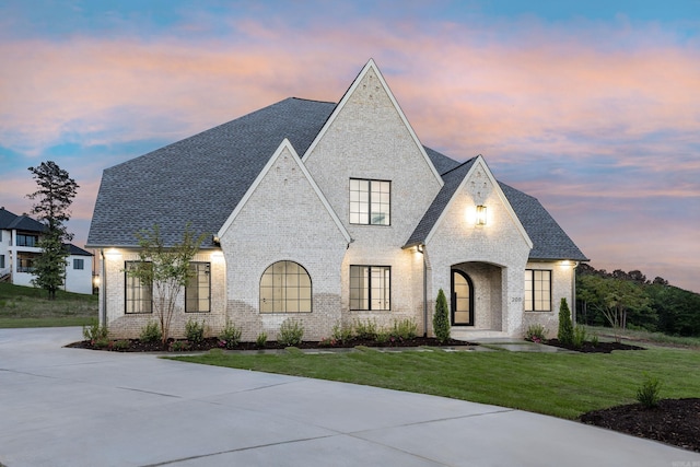 french country style house featuring brick siding, roof with shingles, and a front yard