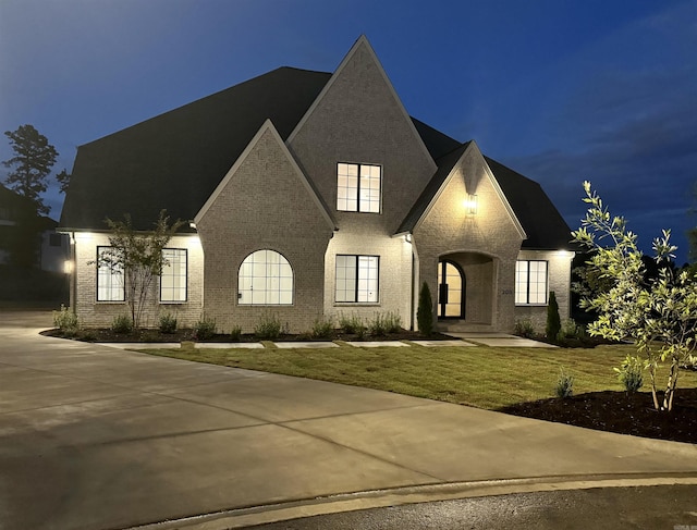 french country style house featuring brick siding and a lawn