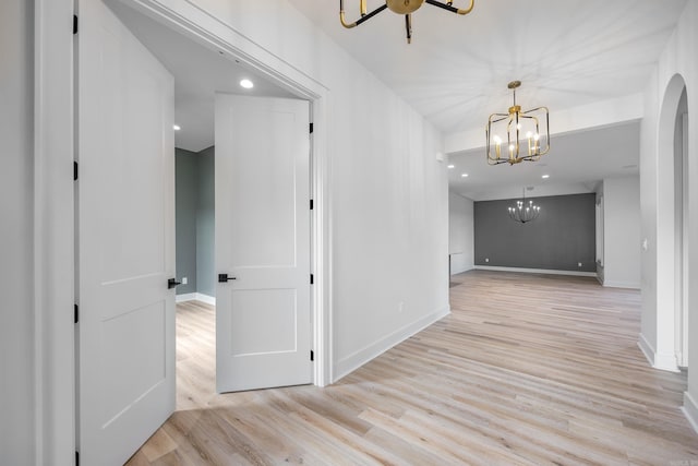 hallway with arched walkways, recessed lighting, light wood-style flooring, a chandelier, and baseboards