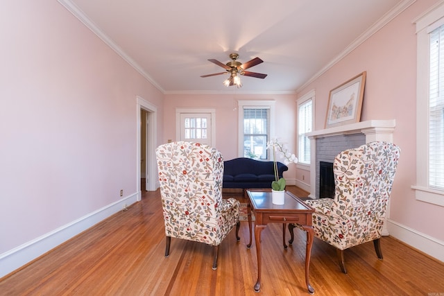 sitting room featuring ceiling fan, wood finished floors, baseboards, ornamental molding, and a brick fireplace