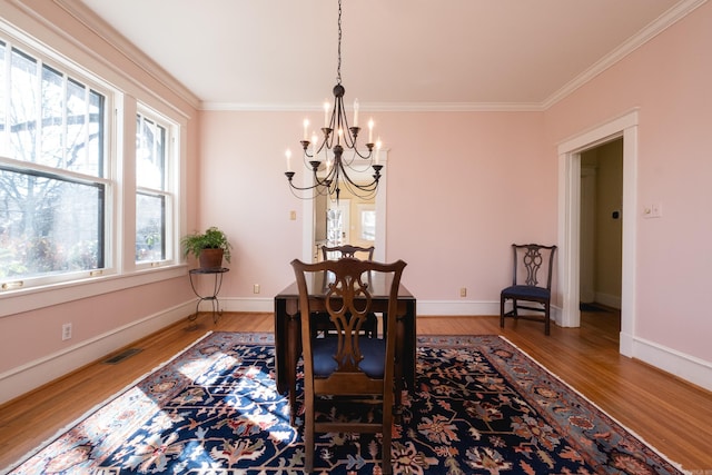 dining space with light wood-type flooring, an inviting chandelier, visible vents, and crown molding