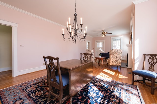 dining space with baseboards, ornamental molding, wood finished floors, and ceiling fan with notable chandelier