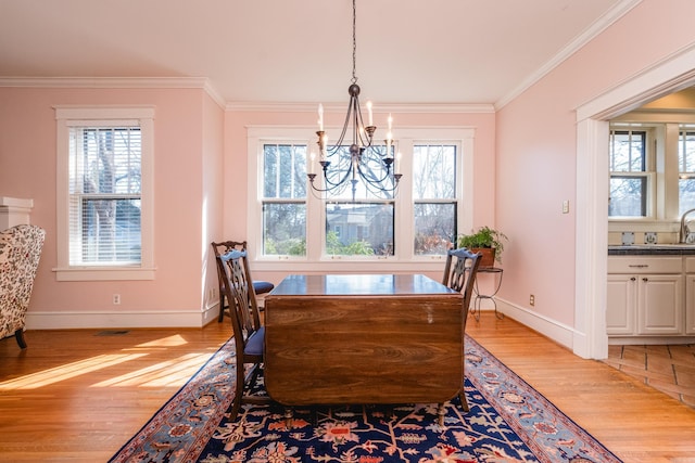 dining space featuring light wood-style floors, baseboards, ornamental molding, and a notable chandelier