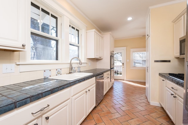 kitchen with brick floor, appliances with stainless steel finishes, ornamental molding, a sink, and baseboards