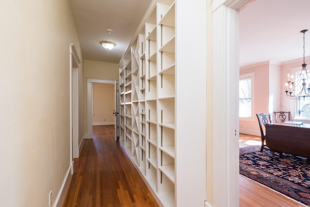 hallway with an inviting chandelier, crown molding, baseboards, and wood finished floors