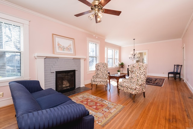 living room featuring ceiling fan with notable chandelier, a fireplace, wood finished floors, baseboards, and ornamental molding