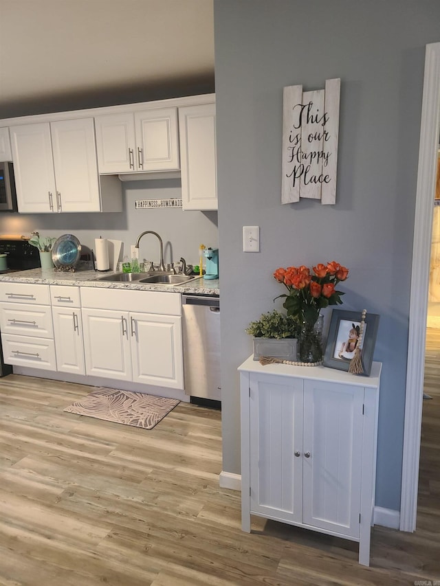 kitchen featuring light wood-style flooring, a sink, baseboards, white cabinets, and appliances with stainless steel finishes