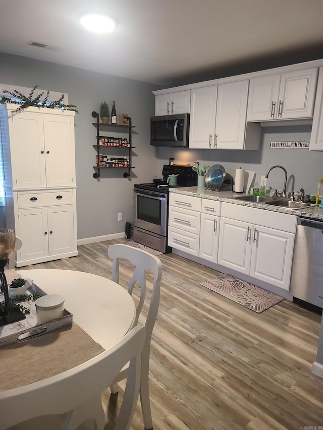 kitchen featuring light countertops, appliances with stainless steel finishes, white cabinetry, a sink, and light wood-type flooring