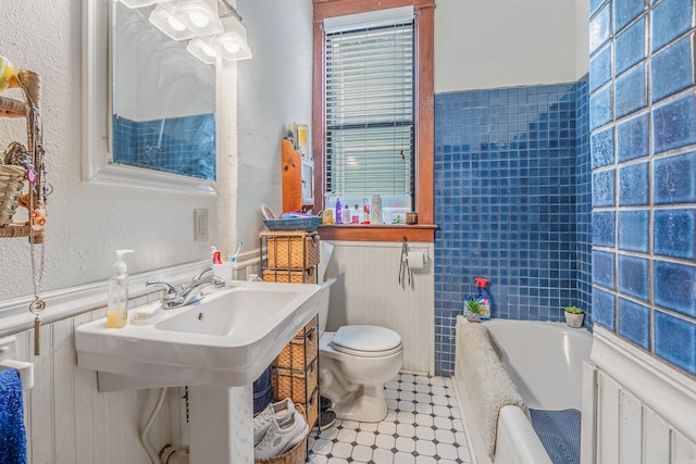 full bath with a wainscoted wall, a textured wall, toilet, and a bath