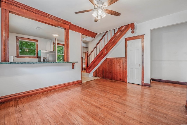 unfurnished living room with visible vents, wainscoting, ceiling fan, wood finished floors, and stairs