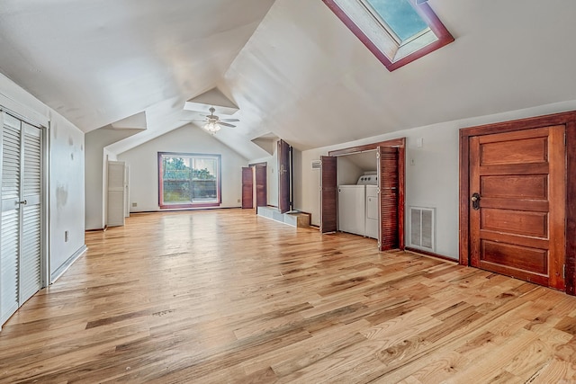 additional living space with light wood-style flooring, vaulted ceiling with skylight, visible vents, and washer and clothes dryer