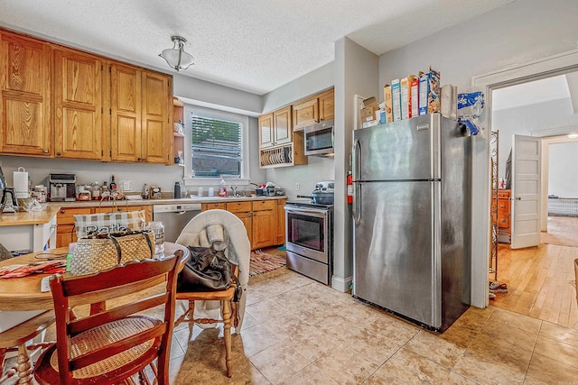 kitchen with light countertops, appliances with stainless steel finishes, brown cabinetry, a sink, and a textured ceiling