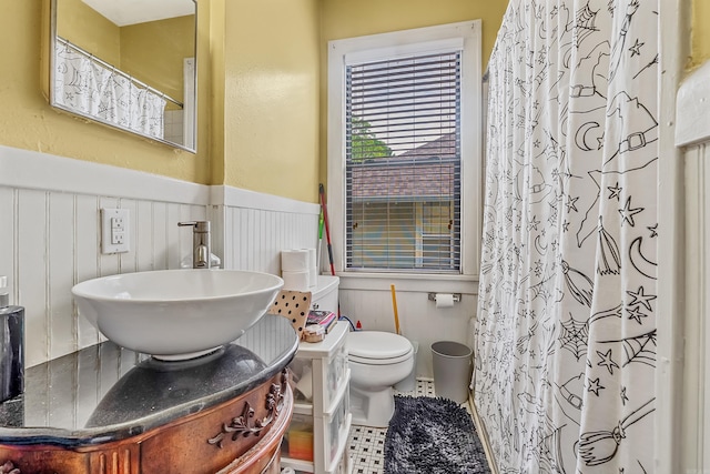 bathroom featuring toilet, a wainscoted wall, a sink, and a shower with shower curtain