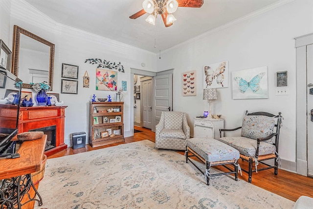 sitting room featuring a fireplace, ornamental molding, a ceiling fan, wood finished floors, and baseboards