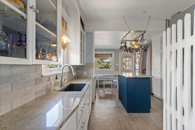 kitchen featuring light stone counters, wood finished floors, a sink, white cabinetry, and backsplash