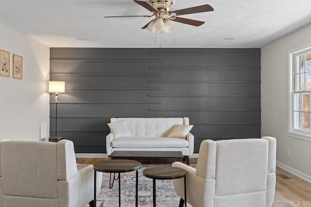 sitting room featuring ceiling fan, light wood-type flooring, baseboards, and a healthy amount of sunlight