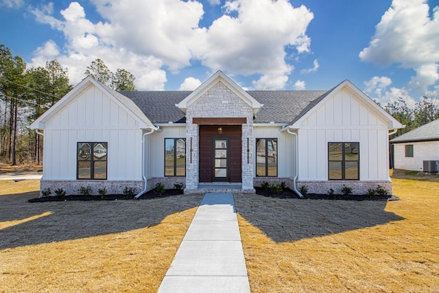 modern farmhouse style home with stone siding, a shingled roof, board and batten siding, and a front lawn