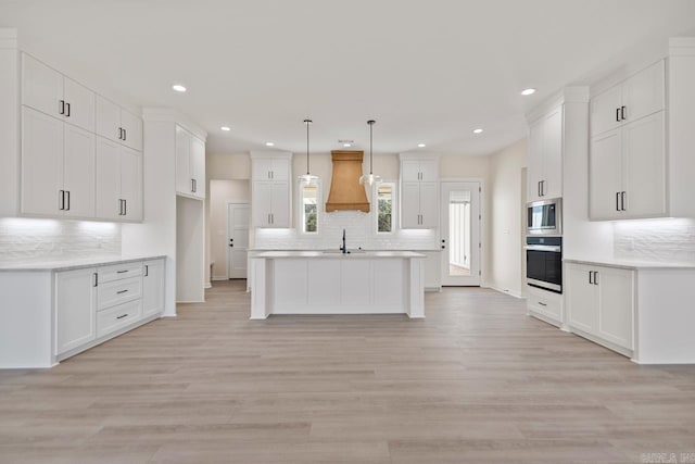 kitchen with light wood-style flooring, oven, a sink, backsplash, and stainless steel microwave