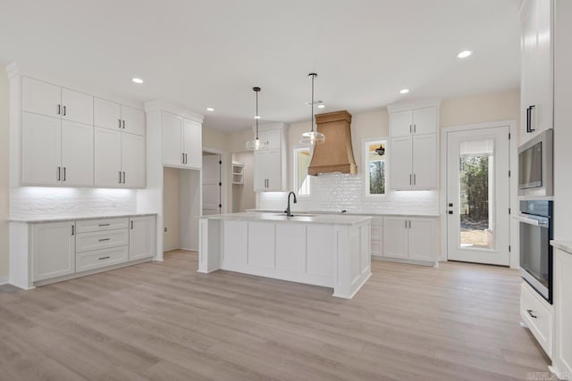 kitchen featuring stainless steel appliances, a sink, light wood-style floors, an island with sink, and custom range hood