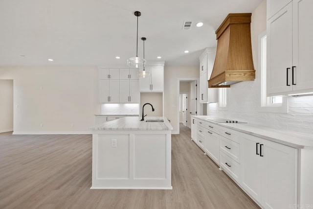 kitchen featuring black electric stovetop, custom exhaust hood, visible vents, light wood-style floors, and a sink