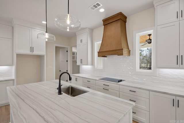 kitchen with black electric cooktop, premium range hood, a sink, visible vents, and white cabinetry