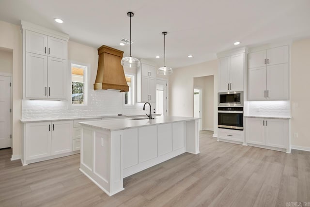 kitchen featuring stainless steel appliances, a sink, light countertops, a center island with sink, and custom range hood