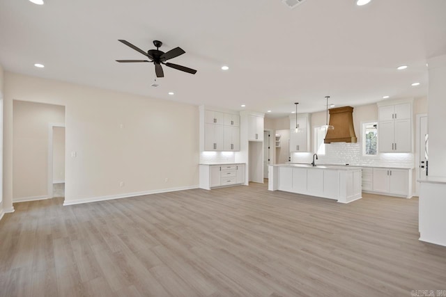 unfurnished living room with light wood finished floors, ceiling fan, a sink, and recessed lighting