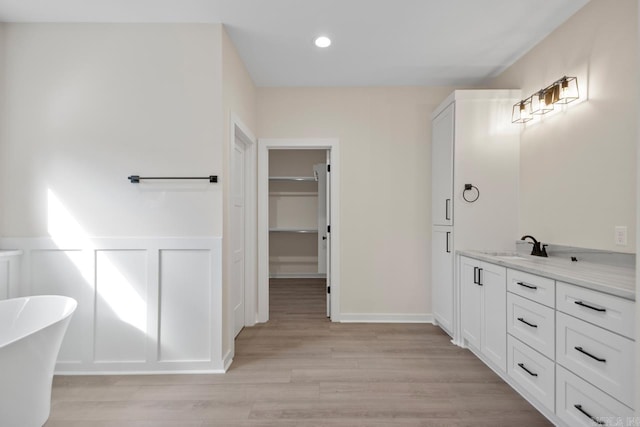 bathroom with a decorative wall, a wainscoted wall, wood finished floors, vanity, and a soaking tub