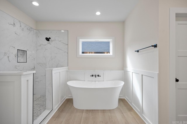 bathroom with a marble finish shower, recessed lighting, wainscoting, wood finished floors, and a freestanding tub