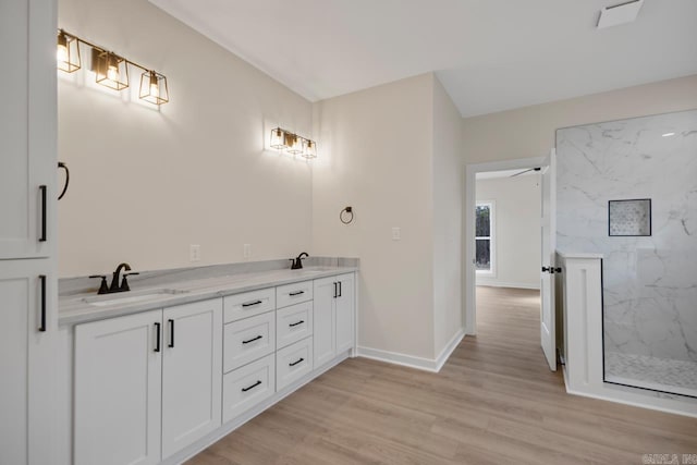 bathroom with a marble finish shower, baseboards, a sink, and wood finished floors