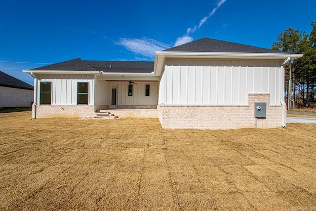 back of house with ceiling fan, a shingled roof, board and batten siding, and a yard