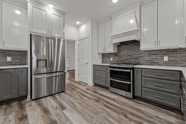 kitchen with wood finished floors, custom exhaust hood, gray cabinets, stainless steel appliances, and light countertops