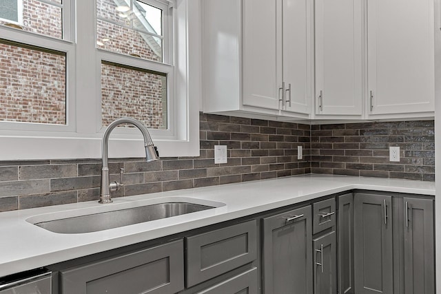 kitchen with backsplash, light countertops, a sink, and gray cabinetry