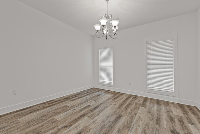 spare room featuring a chandelier, wood finished floors, and baseboards