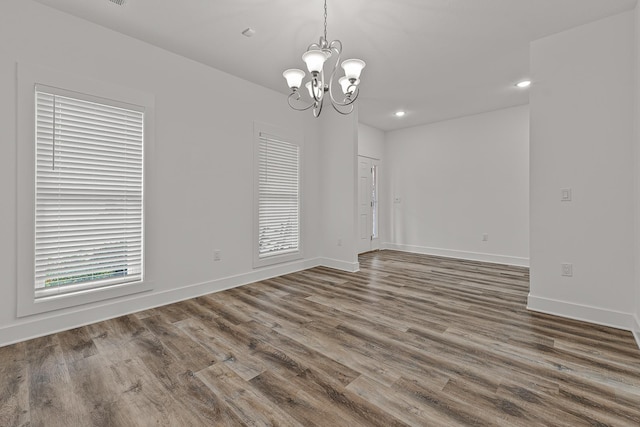 empty room with baseboards, recessed lighting, wood finished floors, and a notable chandelier