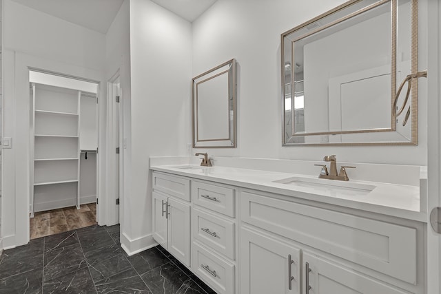 bathroom featuring marble finish floor, double vanity, a sink, and baseboards