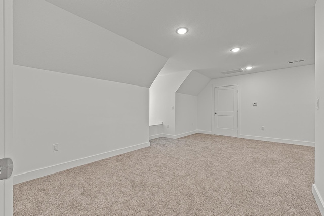 additional living space with light colored carpet, vaulted ceiling, visible vents, and baseboards