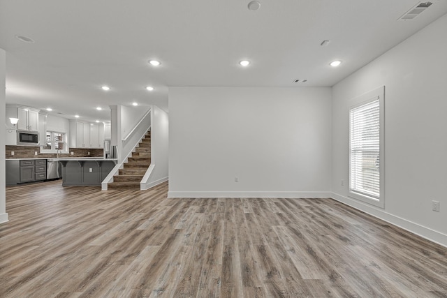 unfurnished living room featuring a healthy amount of sunlight, stairway, visible vents, and light wood finished floors