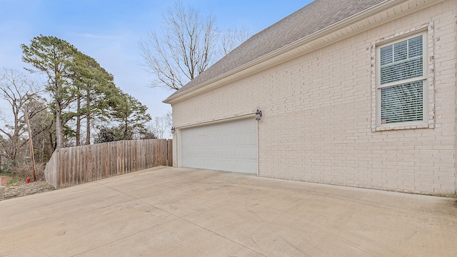 view of property exterior featuring brick siding, driveway, an attached garage, and fence