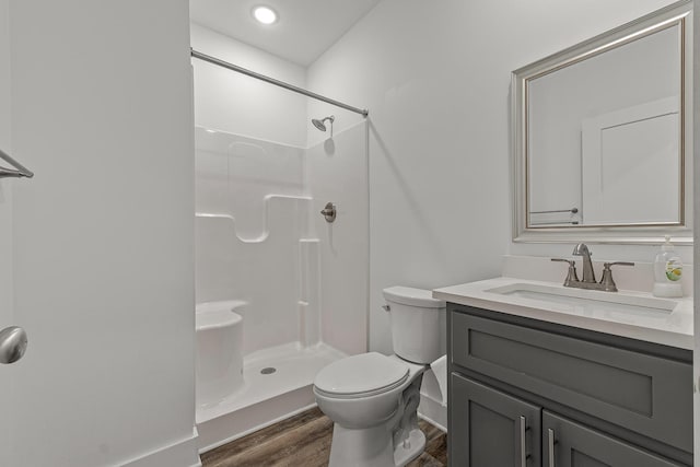 bathroom featuring toilet, walk in shower, wood finished floors, and vanity