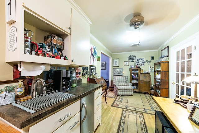 kitchen with light wood finished floors, white cabinetry, ornamental molding, and a sink