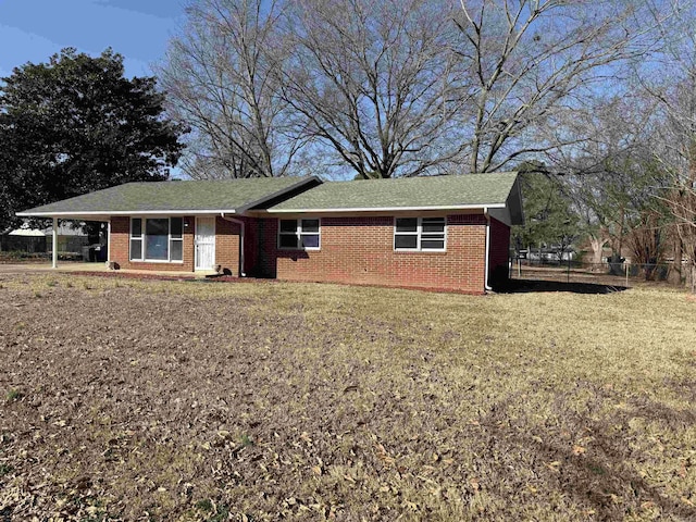 ranch-style home featuring a front yard, fence, a carport, and brick siding