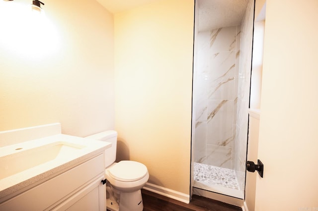 bathroom with toilet, wood finished floors, vanity, baseboards, and a marble finish shower