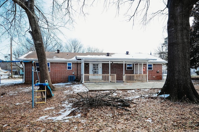 snow covered house with covered porch, brick siding, and central AC