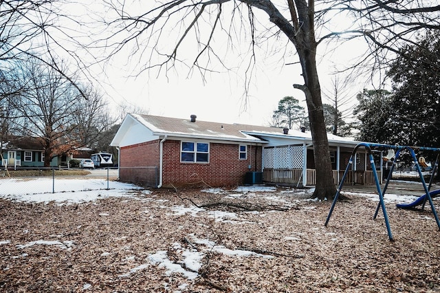 snow covered back of property with brick siding, fence, and a playground