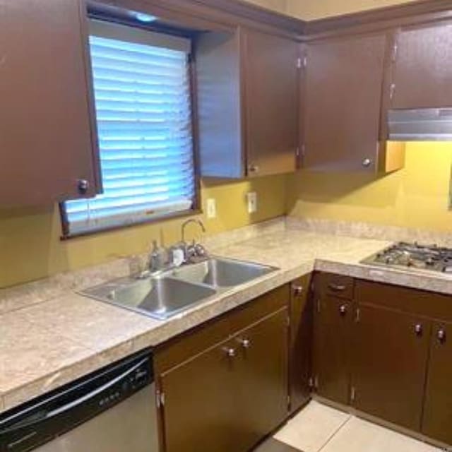 kitchen featuring light tile patterned flooring, a sink, stainless steel appliances, light countertops, and under cabinet range hood