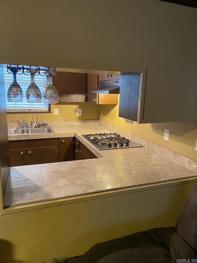 kitchen featuring under cabinet range hood, a sink, light countertops, and stainless steel gas cooktop