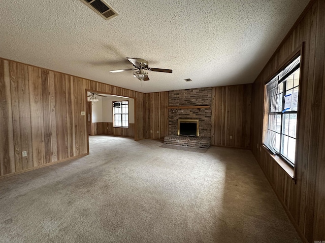 unfurnished living room featuring light carpet, wood walls, a fireplace, and a textured ceiling