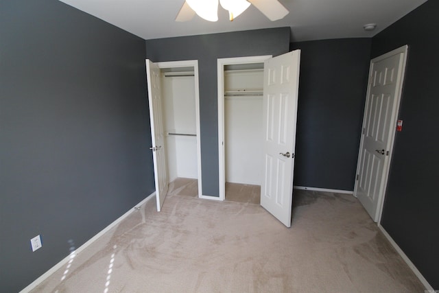 unfurnished bedroom with ceiling fan, baseboards, two closets, and light colored carpet