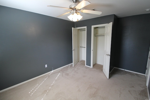 unfurnished bedroom with ceiling fan, light carpet, two closets, and baseboards